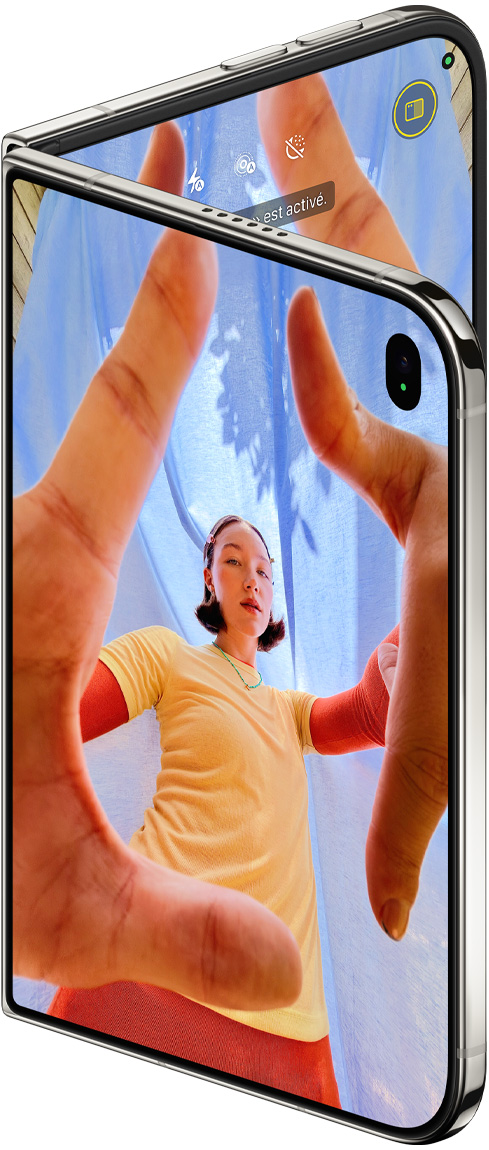 iPhone Duo, couleur blanc stellaire, légèrement ouvert, app Caméra sur l’écran externe avec caméra avant Center Stage, écran interne affichant la photothèque de l’app Photos