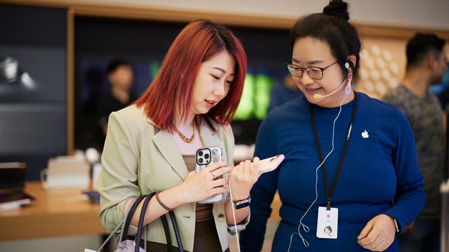 Zákazník drží růžový iPhone 15 a hovoří se zaměstnancem Applu v prodejně Nanjing East.