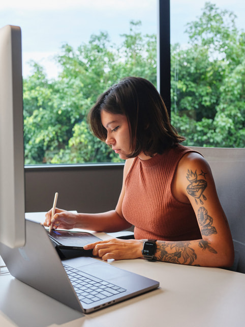 Maria Clara Reis Guimarães desenhando no iPad com o Apple Pencil enquanto usa um MacBook Pro. 