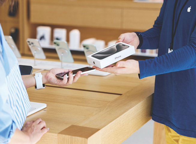 Una imagen que representa el programa Apple Trade In muestra a un cliente intercambiando su antiguo iPhone por uno nuevo en una caja.