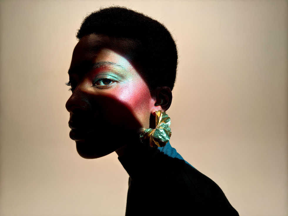 Une personne au maquillage coloré pose dans la pénombre sur une photo prise avec un iPhone 16 Pro.