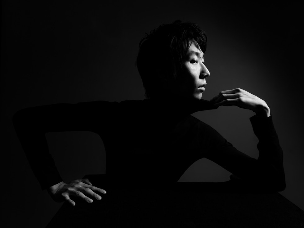 Une personne pose en intérieur sur une photo en noir et blanc prise avec un iPhone 16 Pro.