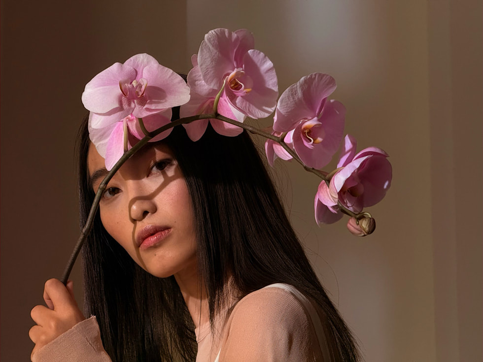 Une personne tient une branche d’orchidée rose sur une photo prise avec un iPhone 16 Pro.