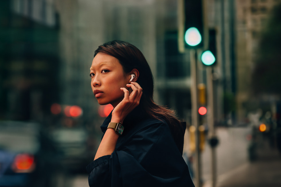 En person som har på seg Apple Watch Series 10 og AirPods 4 i ørene, står på en bygate.