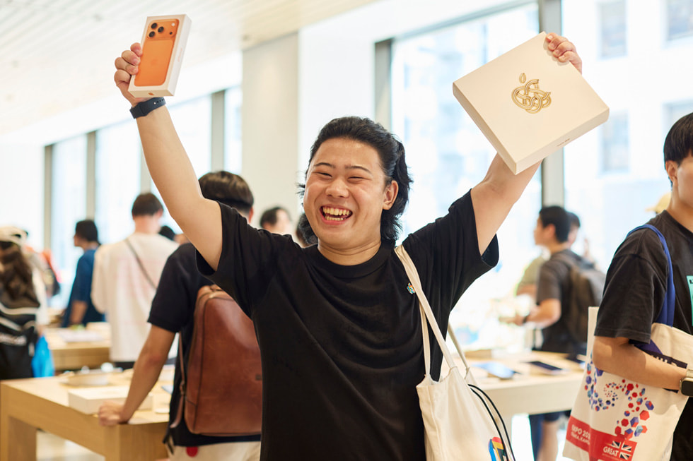 Ein Kunde mit einem iPhone 17 Pro in Cosmic Orange in der einen und einem Apple Ginza Erinnerungsgeschenk in der anderen Hand.