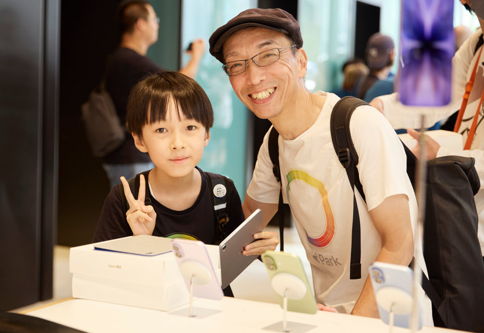 Ein Kind und eine erwachsene Person mit einem iPad neben einem iPhone 17 Ausstellungstisch in Apple Ginza.