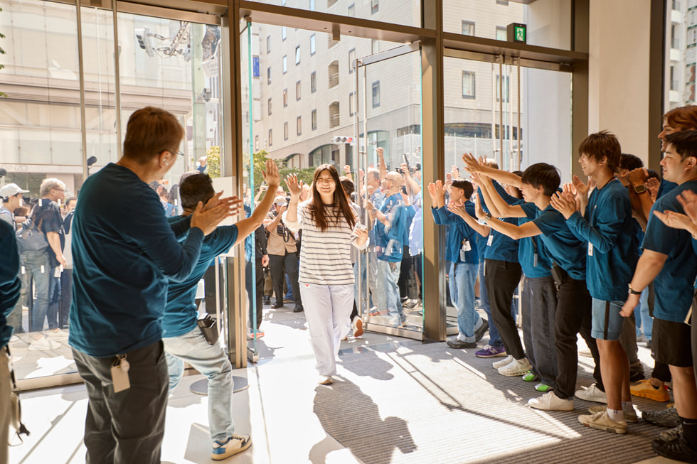 Eine lächelnde Kundin beim Betreten von Apple Ginza, während das Team jubelt.