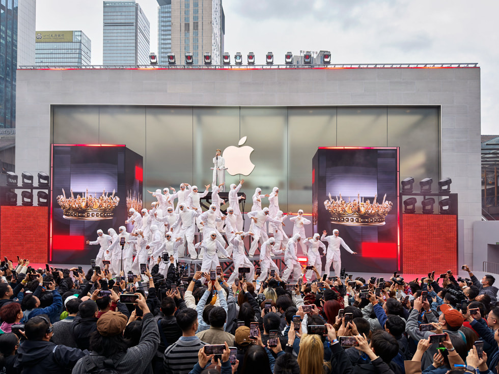 Bailarines con trajes blancos forman una pirámide mientras Chris Lee canta en la cúspide en Apple Taikoo Li Chengdu, en China.