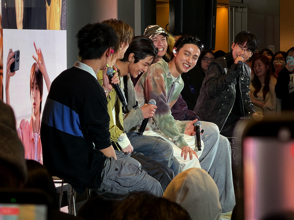 Imagen de los integrantes de la banda CORTIS sonriendo y sentados con micrófono en mano en Apple Myeongdong, en Seúl.