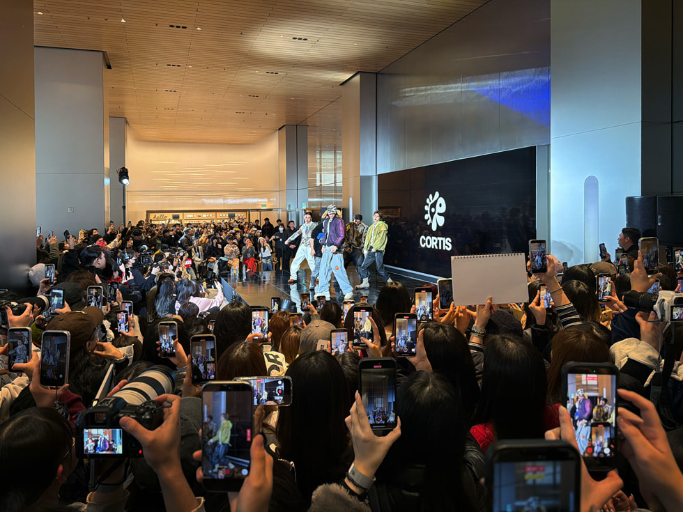 Desde la perspectiva del público, se observa a los fans con cámaras y dispositivos iPhone durante la presentación de CORTIS en un escenario de Apple Myeongdong, en Seúl.