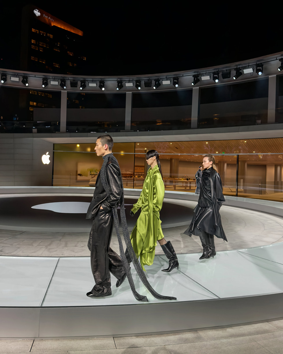 Dos personas vestidas de negro y una vestida de verde desfilan en una pasarela circular en Apple Jing’an.