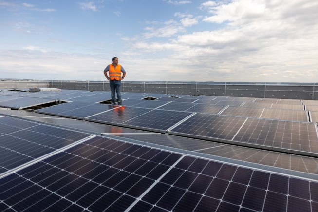 Un conjunto de paneles solares ubicados cerca de una comunidad y montañas con bosques.