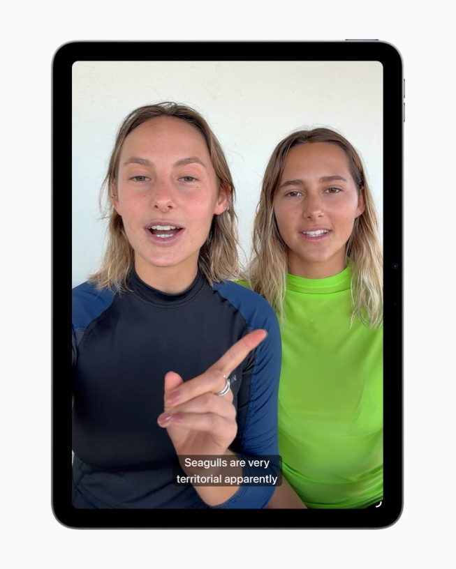 Un cuadro de video en el iPad muestra a dos personas hablando, con subtítulos generados que aparecen en la parte inferior de la pantalla.