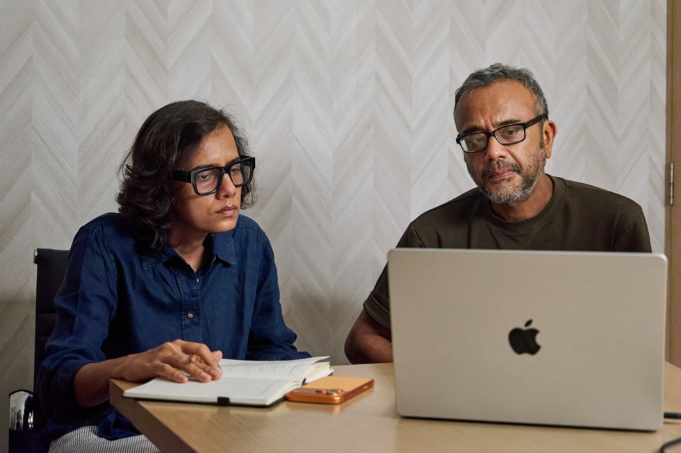 Dhritisree Sarkar y un colega sentados en una mesa, mirando la pantalla de una MacBook Pro, y un iPhone 17 Pro Max apoyado sobre la mesa.