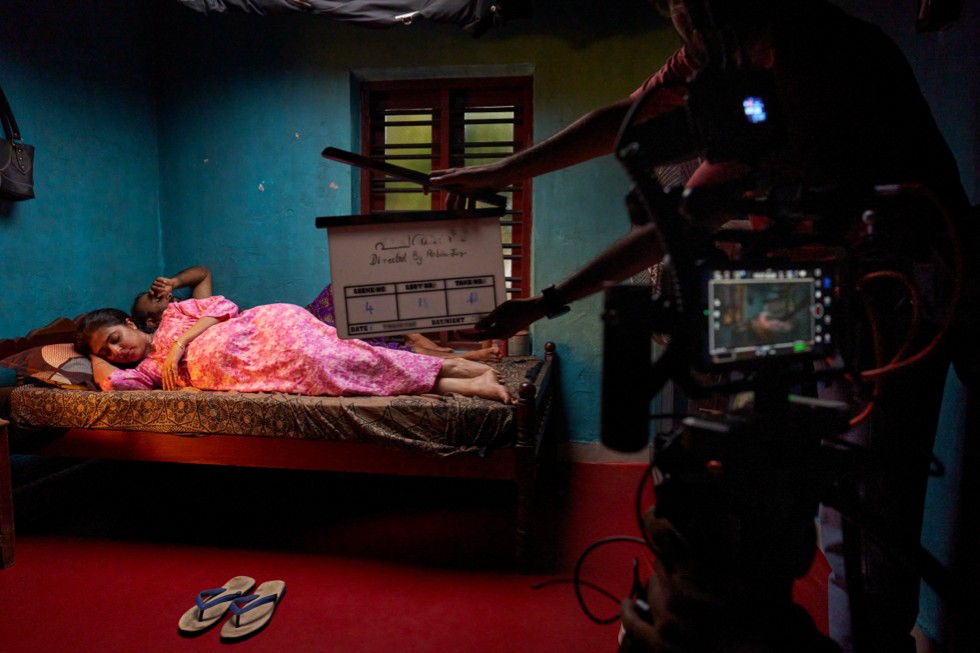 Un set de filmación con una persona acostada en una habitación con poca luz, donde se ve el equipo de grabación.