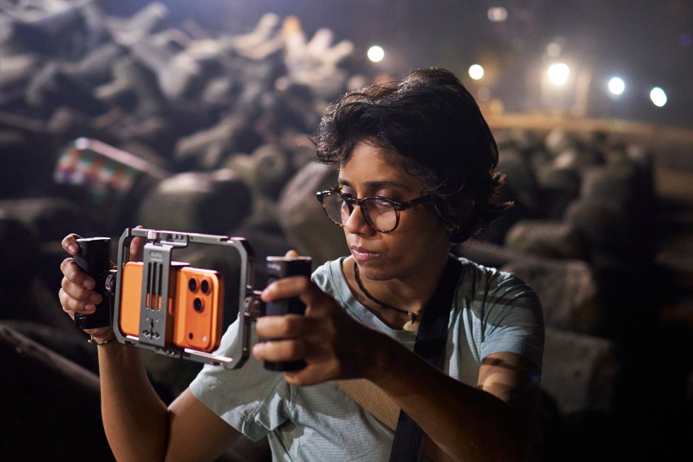 Shreela Agarwal sostiene un soporte de grabación con un iPhone 17 Pro Max instalado mientras filma de noche al aire libre.