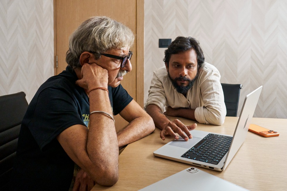 Ritesh Sharma sentado en un escritorio junto con un miembro de su equipo, con una MacBook Pro y un iPhone 17 Pro Max apoyado sobre el escritorio.