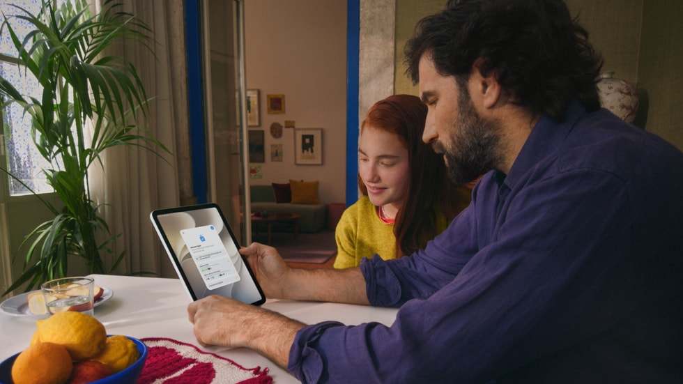 Un hombre y una niña están sentados junto a una mesa de madera, interactuando con el iPad.