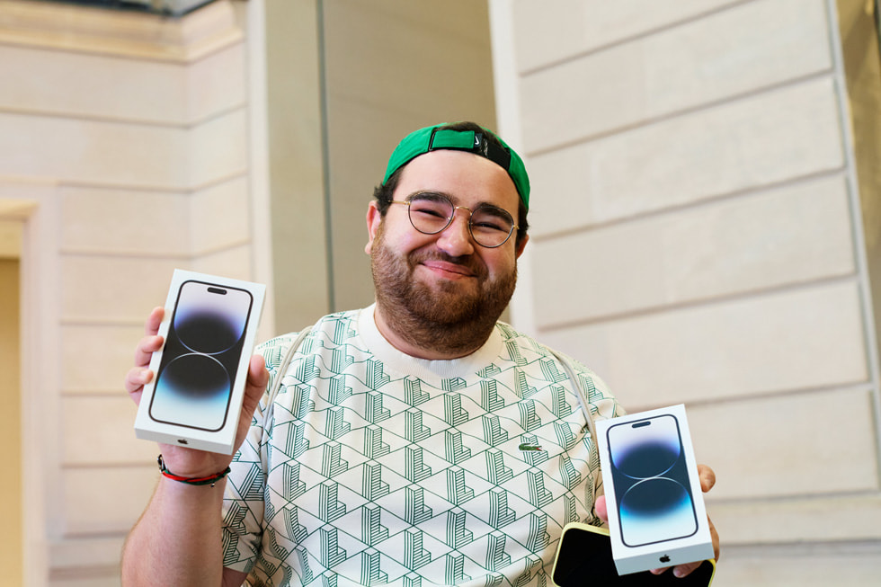 En kund står utanför Apple Champs-Élysées och tittar på fönsterskyltning med olika iPhone-enheter.