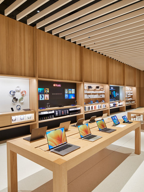 Ett bord med Mac-datorer och en vägg med produkter på Apple Tysons Corner.