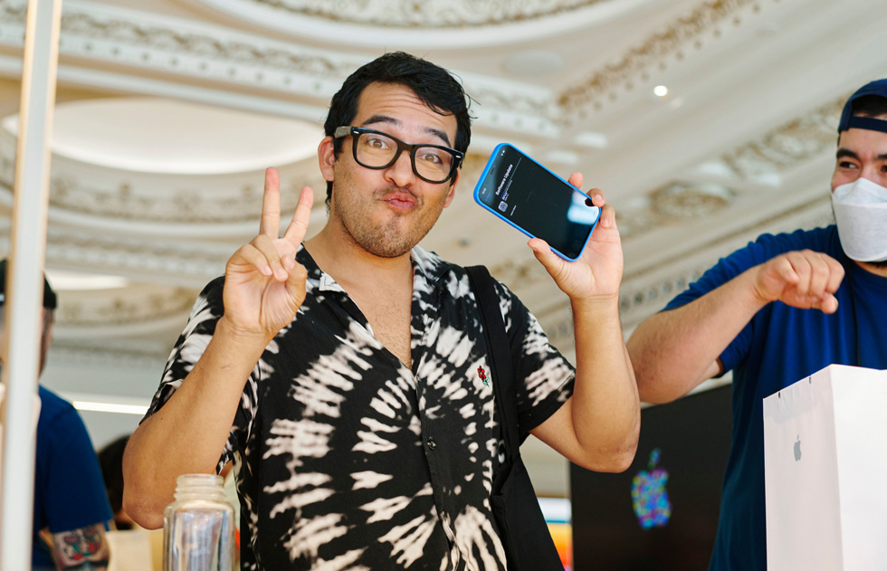 En kunde i Apple Tower Theatre laver et peace-tegn med den ene hånd og holder sin iPhone 12 i den anden.