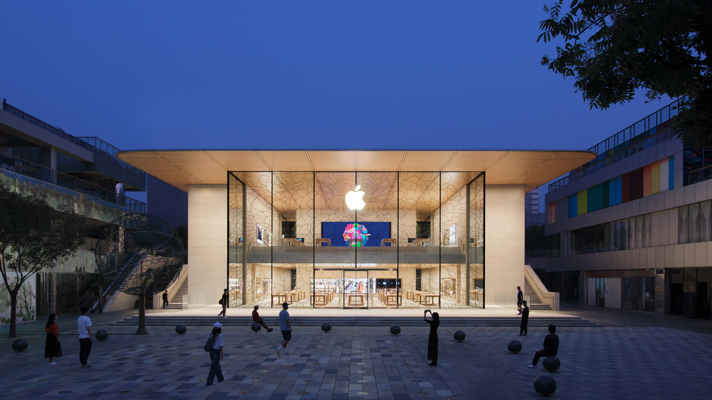 مشهد خارجي لواجهة متجر Apple سانليتون عند غروب الشمس يُظهر الإضاءة الداخلية للمتجر التي تُبرز انسيابية التصميم وشفافيته.