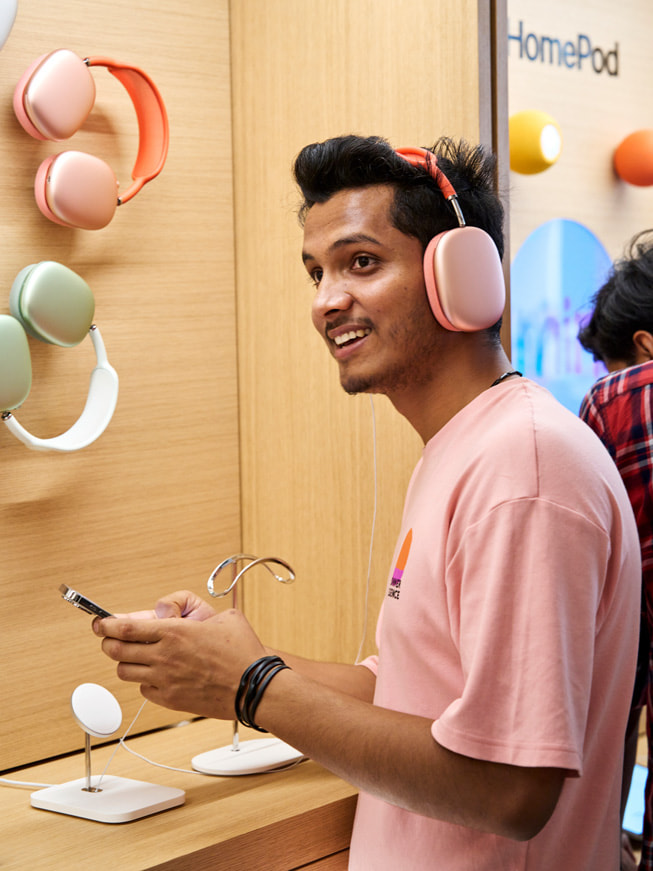 En kund provar AirPods Max framför en vägg där hörlurarna visas upp.