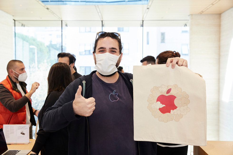 Apple tişörtlü bir adam elindeki Apple logosunu göstererek baş parmağıyla çok iyi işareti yapıyor.