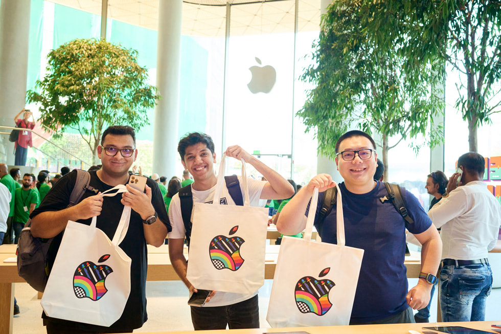 Klienci pozujący z torbami zakupowymi, na których widać logo Apple. 