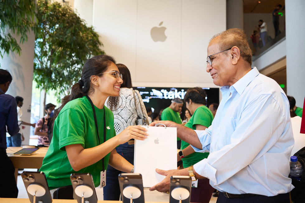 Członkini zespołu Apple BKC wręcza klientowi jego zakupy. 