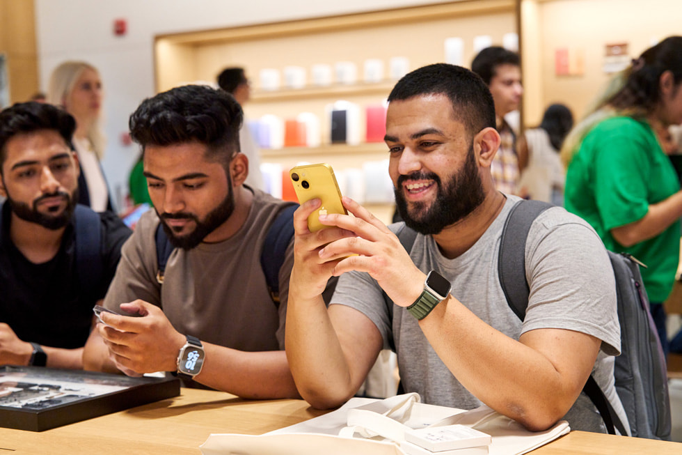 En kund vid ett av borden inne i Apple Saket tittar närmare på en iPhone 14 i den nya gula färgen.