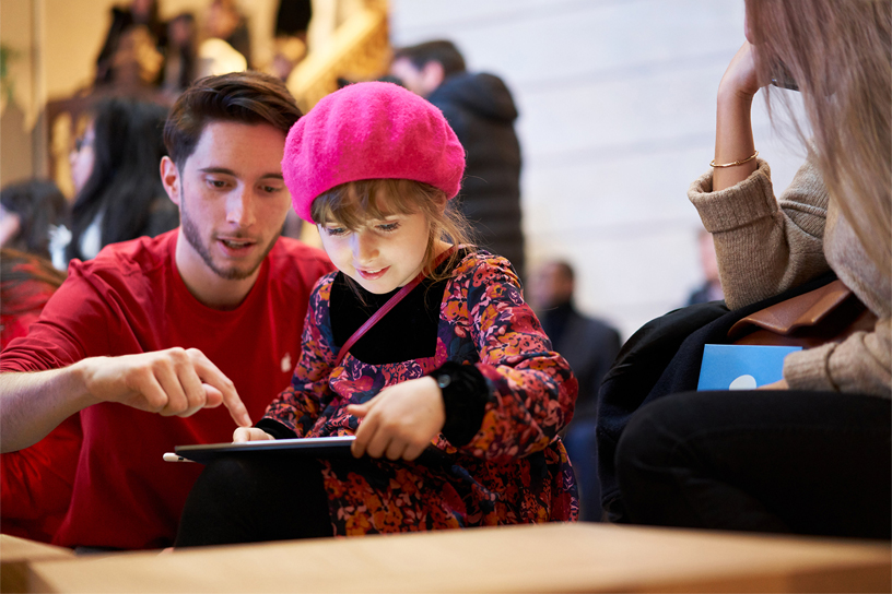 Apple ekibinin bir üyesi küçük bir kıza iPad kullanmayı öğretiyor.
