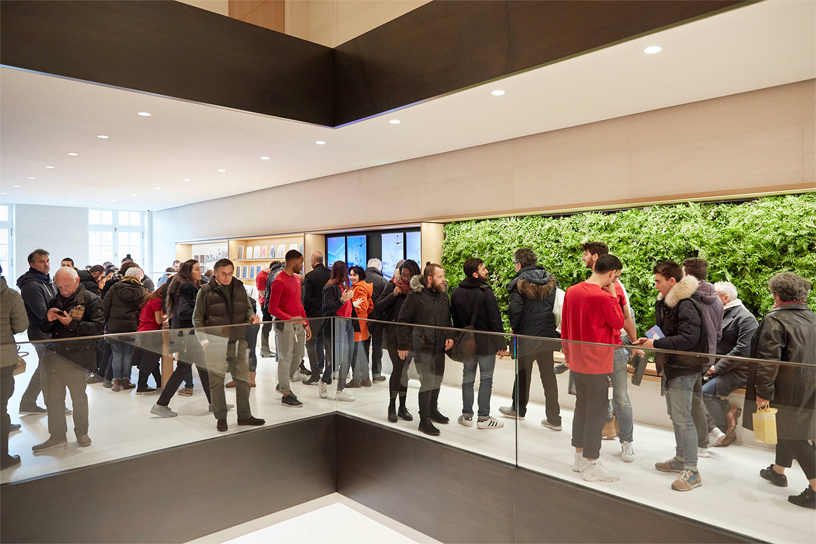 Ekip üyeleri ve müşteriler Apple Champs-Élysées’deki yeşil bir duvarın önünde duruyor.