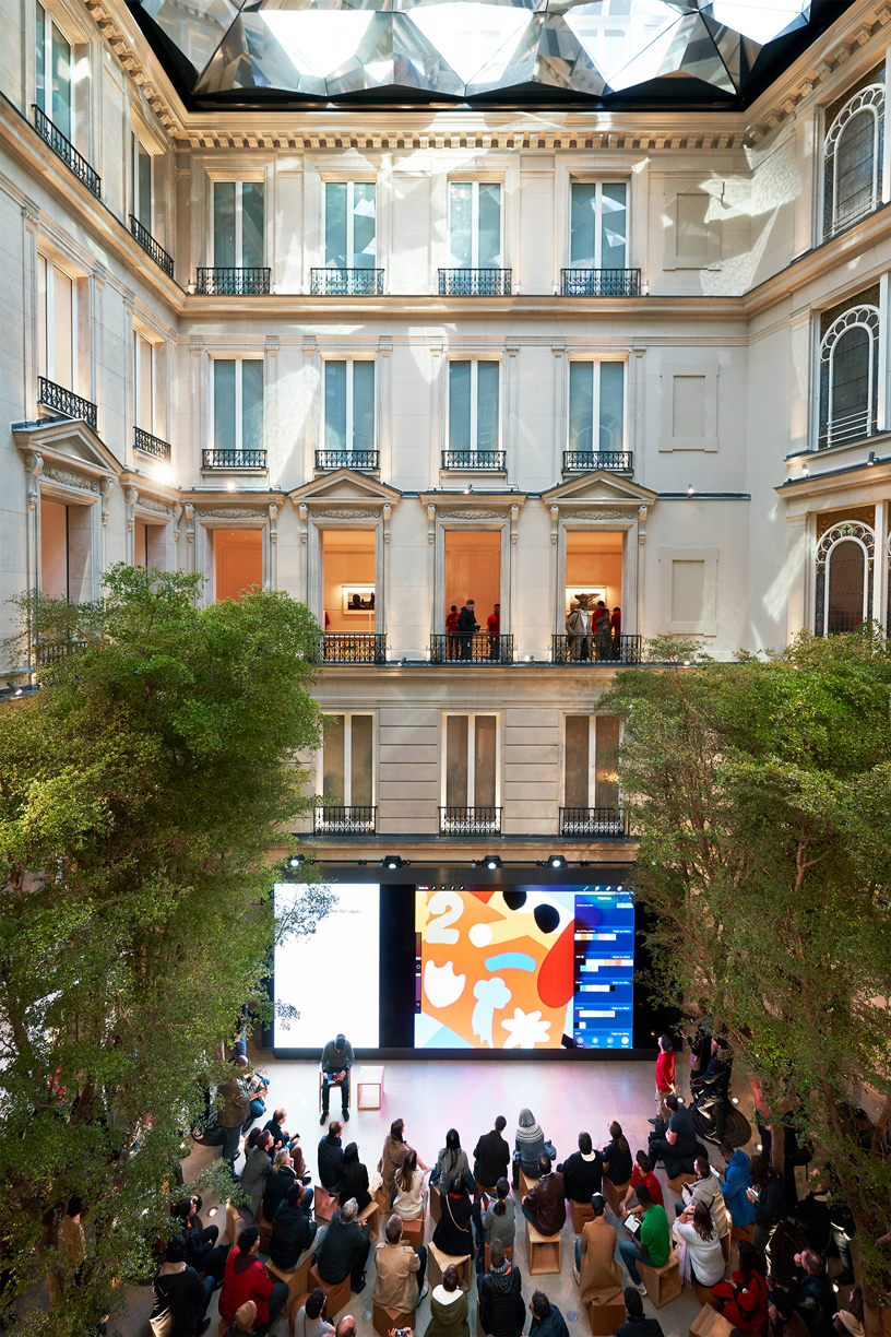 Kalabalık bir müşteri topluluğu Apple Champs-Élysées’deki Forum alanında oturuyor.