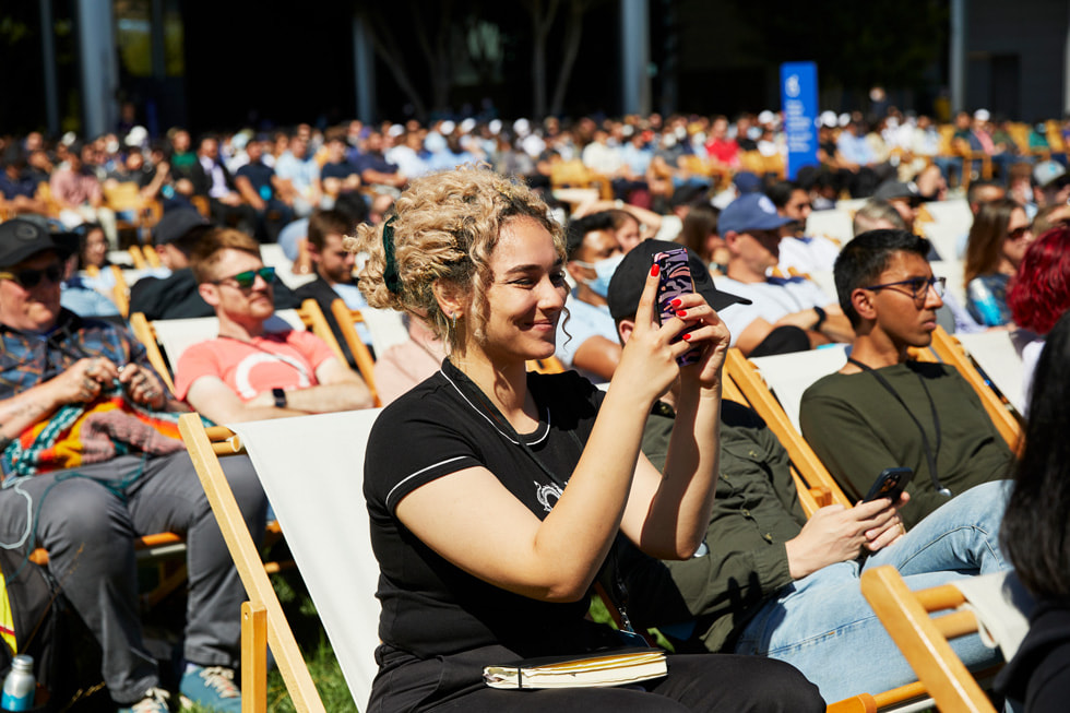 Deltakere ser hovedpresentasjonen for WWDC22 utenfor Caffè Macs i Apple Park.