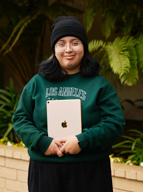 Et portrett av Angela Ibarra, en elev ved Exceptional Minds. Angela har på seg en grønn genser med teksten «Los Angeles, California», gjennomsiktige briller og en svart lue.