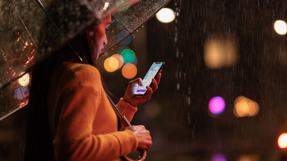 Yağmurun altında elinde iPhone Xs tutan kadın.