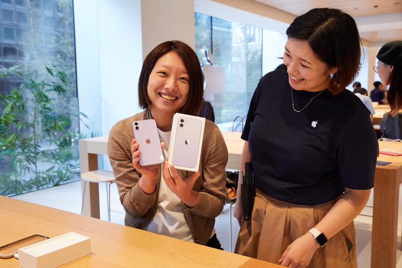 Apple丸の内の店内で、Appleチームメンバーと並び、iPhone 11 とiPhoneの箱を持ち上げてみせるお客様。