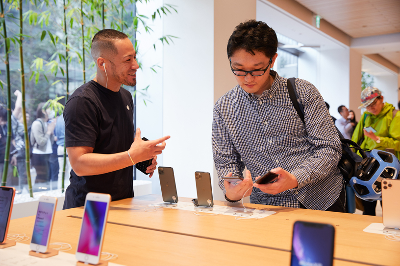 Apple丸の内の店内で、iPhone 11 Pro をチェックするお客様に話しかけているAppleチームメンバー。