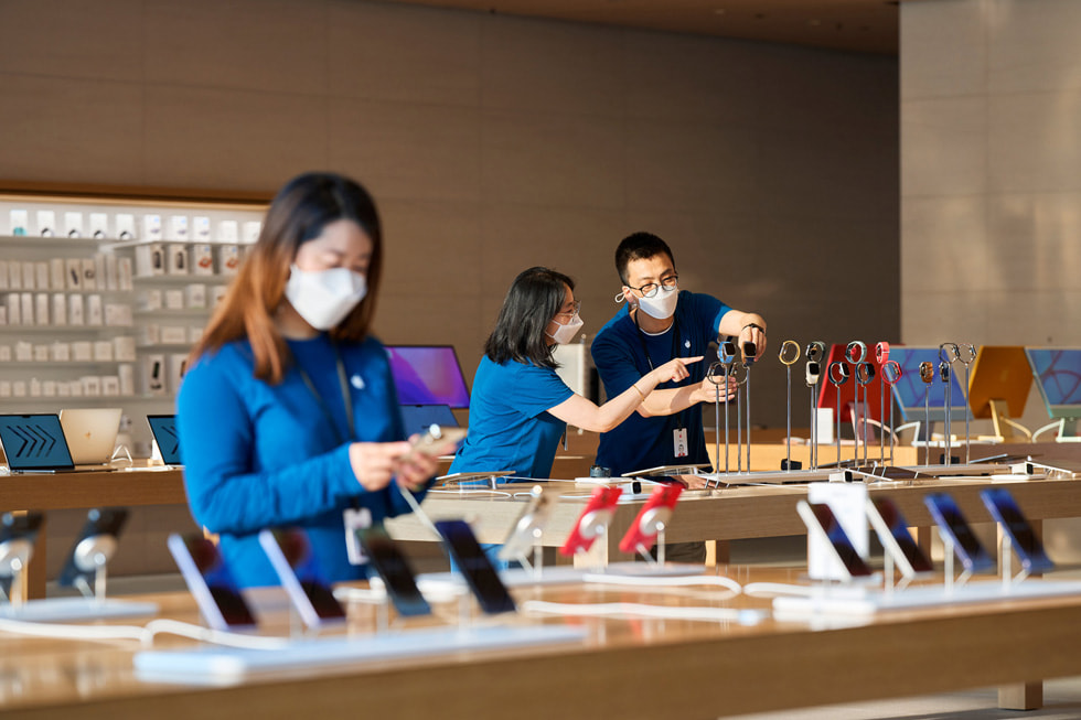 En Apple Sanlitun-medarbetare tittar på iPhone medan två medarbetare justerar Apple Watch-skyltningen i bakgrunden.