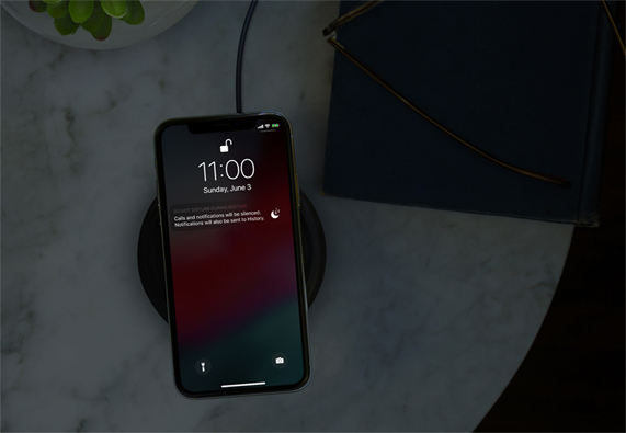 暗い部屋でワイヤレス充電器に置かれたiPhone。おやすみモードが表示されている。