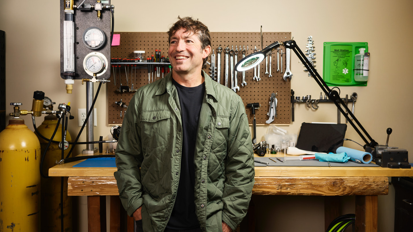 様々なツールとスキューバ機材が並んだ作業台の前に立つ、Huish OutdoorsのCEOであるマイク・ヒューイッシュ氏。 