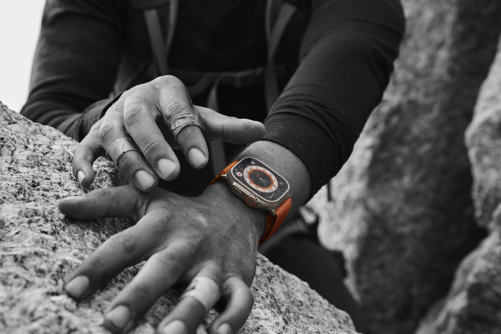 Bir kayanın üzerinde duran, bandajlı iki elin yakın plan çekim fotoğrafında bileklerden birine takılmış Apple Watch Ultra gösteriliyor. 