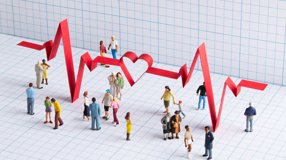 Büyük bir EKG sinyali grafiğiyle çevrelenmiş kişileri üstten gösteren resim. 