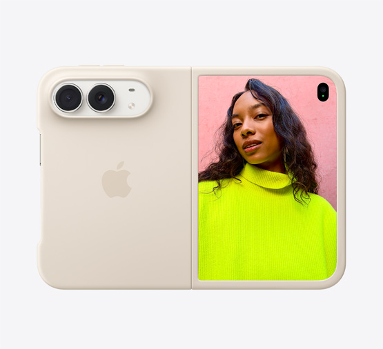 Ustawiony poziomo i rozłożony iPhone Duo w kolorze gwiezdnej bieli z silikonowym etui w kolorze piasku, w lewym górnym rogu widoczny jest system dwóch aparatów Fusion, etui zakrywa tył obudowy i zewnętrzną krawędź wyświetlacza przedniego, z prawej strony na wyświetlaczu zewnętrznym widać osobę stojącą pod zachmurzonym niebem