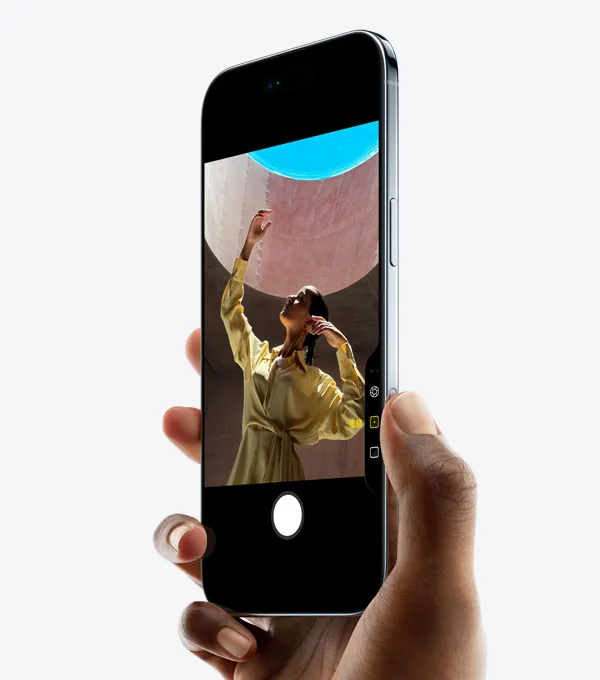 一隻手握著 iPhone Air,拇指按著相機控制按鈕,機身正面側斜展示纖薄外型、動態島、側邊按鈕