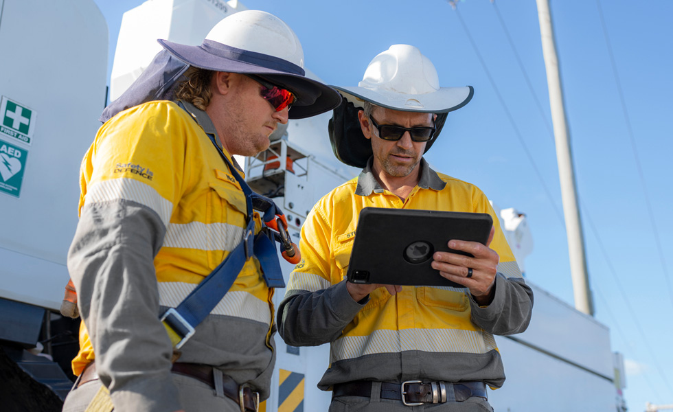 Due tecnici impegnati sul campo collaborano su un iPad accanto a un mezzo di servizio