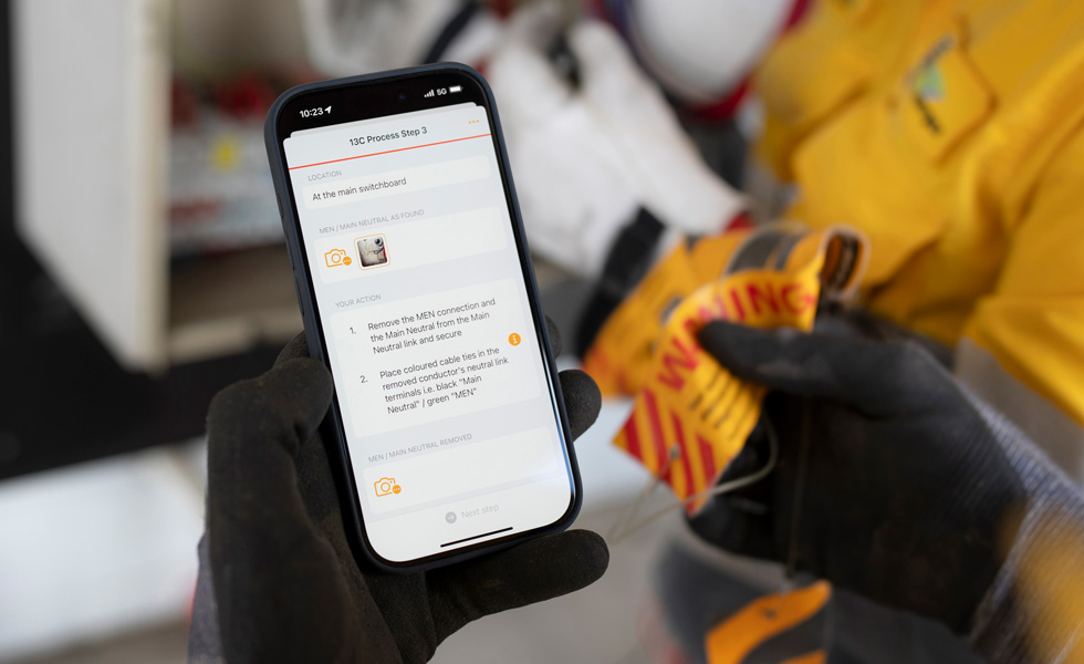 Due mani tengono un iPhone che indica come eseguire una verifica del quadro elettrico, con le parole “13C Process Step 3” scritte sullo schermo