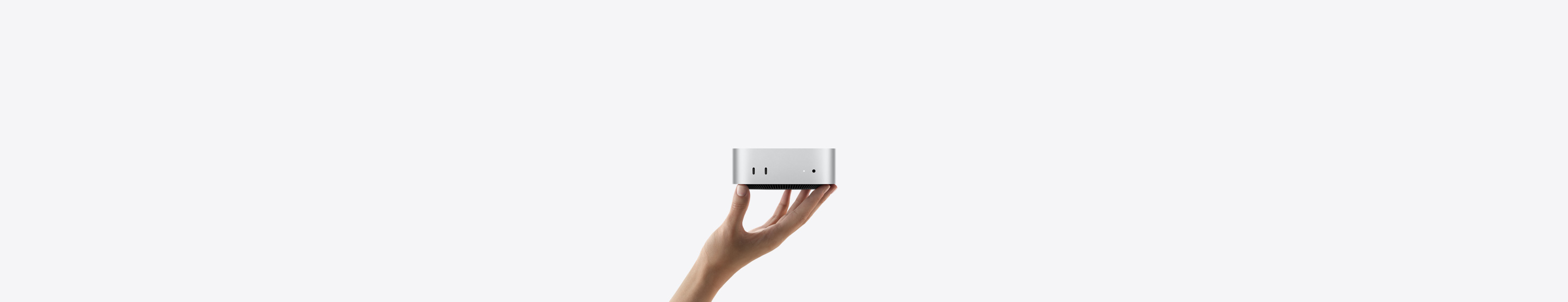 Imagem da frente do Mac mini equilibrado na ponta dos dedos de uma mão esticada. A parte da frente mostra duas portas Thunderbolt, uma luz indicadora de status e a entrada para fones de ouvido. A base na cor preta é afunilada, com parte superior plana, laterais arredondadas e bordas retas