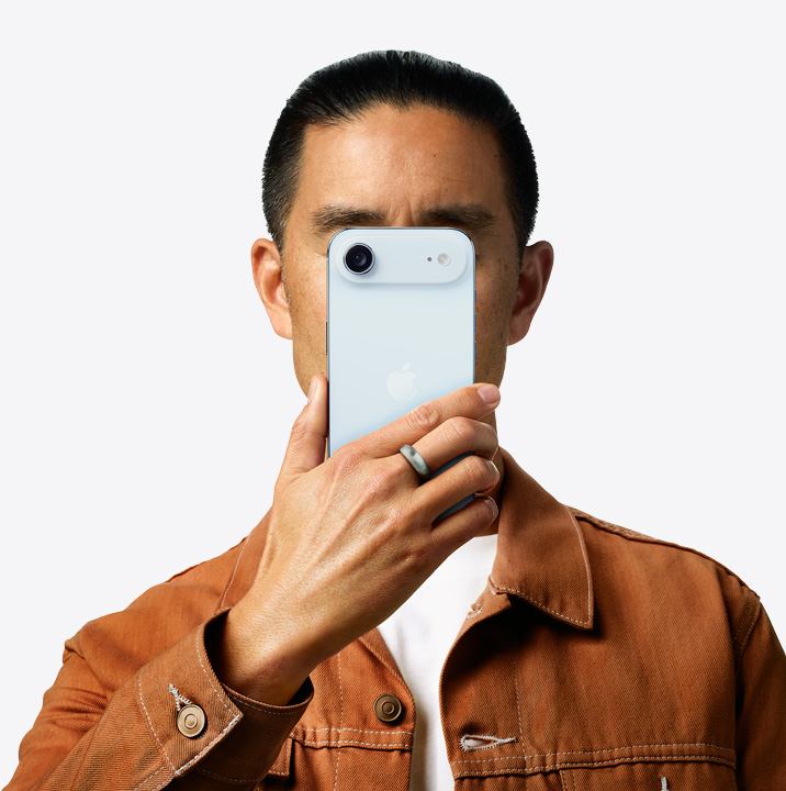 A person holding iPhone 16 in pink finish in front of her face showing back exterior, dual camera system on left top corner.